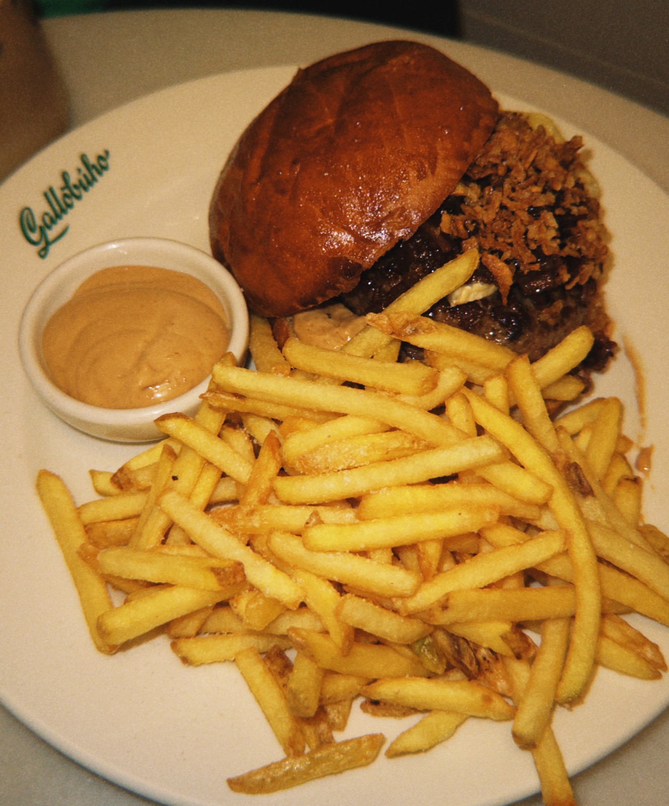 Hamburguesa con patatas en un plato con el logo de Gallobúho